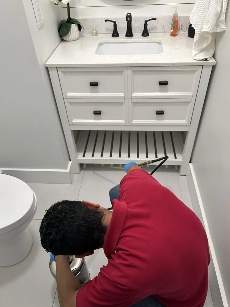 PC New Bedford technician treating the plumbing void under a bathroom vanity during an interior visit